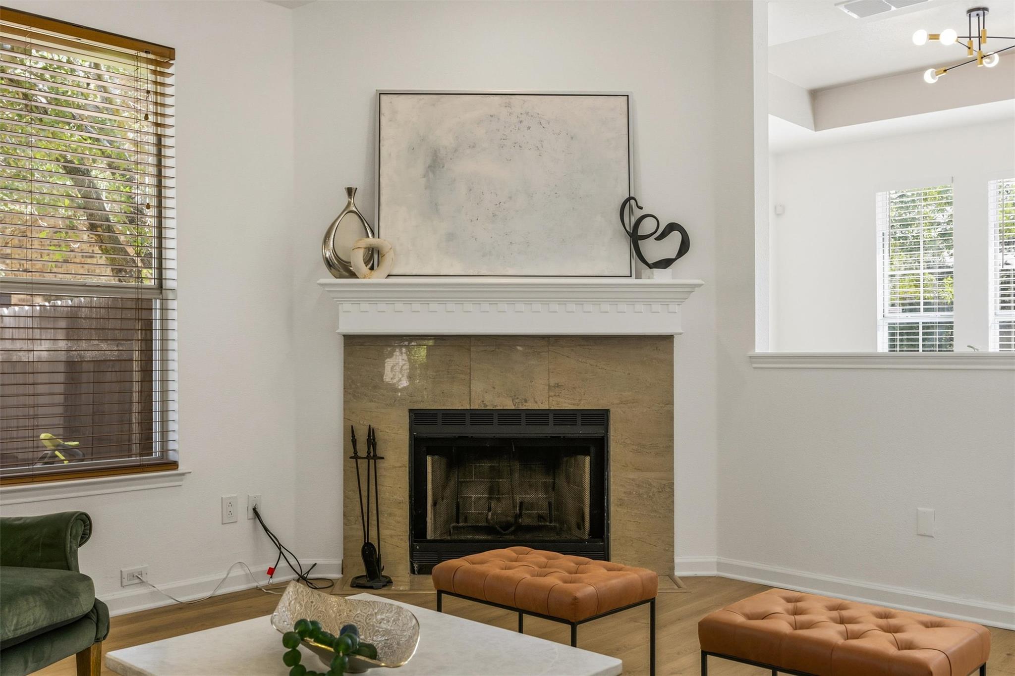 Living room with a tan stone fireplace, white mantel, and tufted leather ottomans.