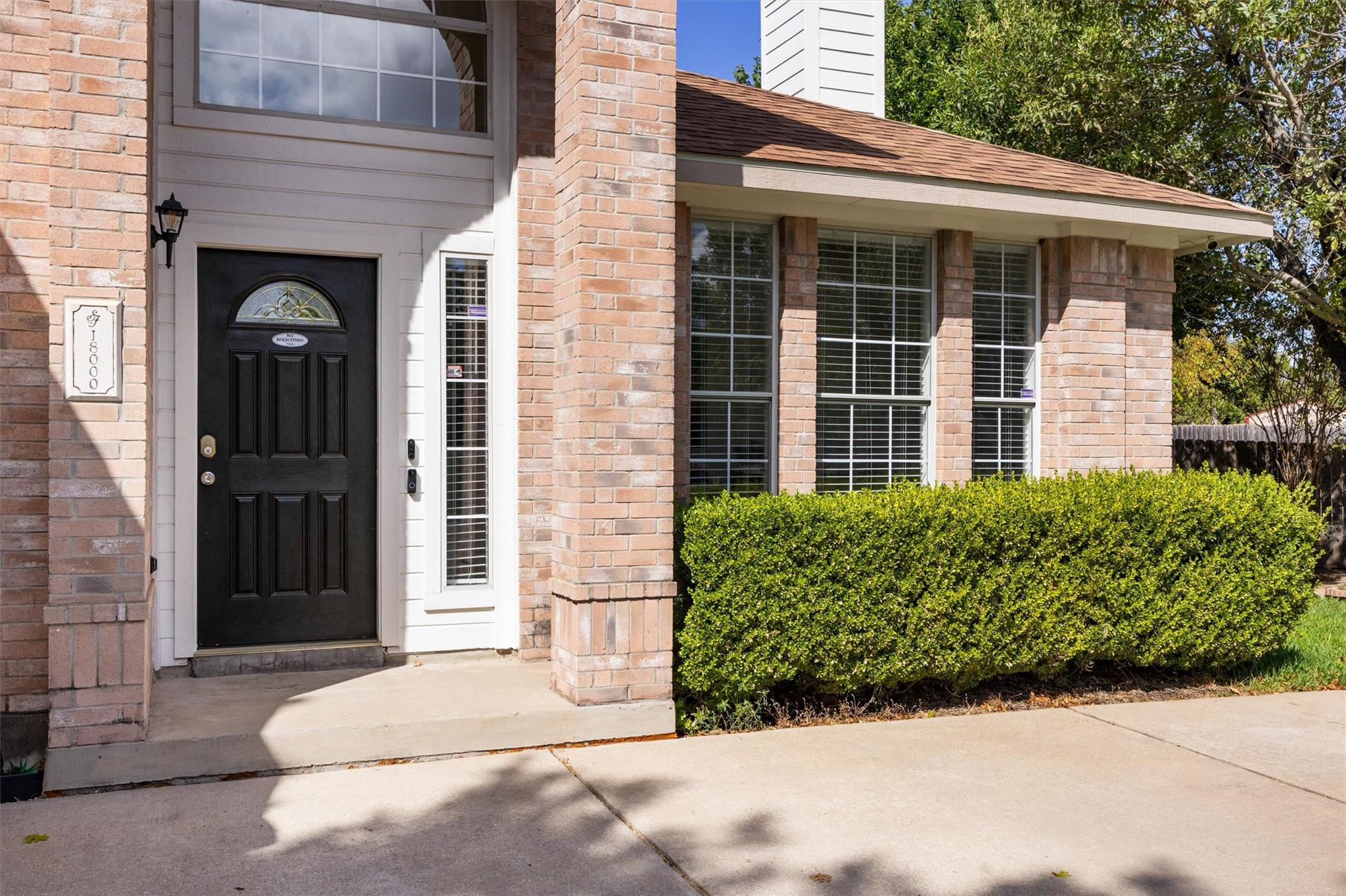 Brick home entrance with a black door, tall windows, and a neatly trimmed hedge.