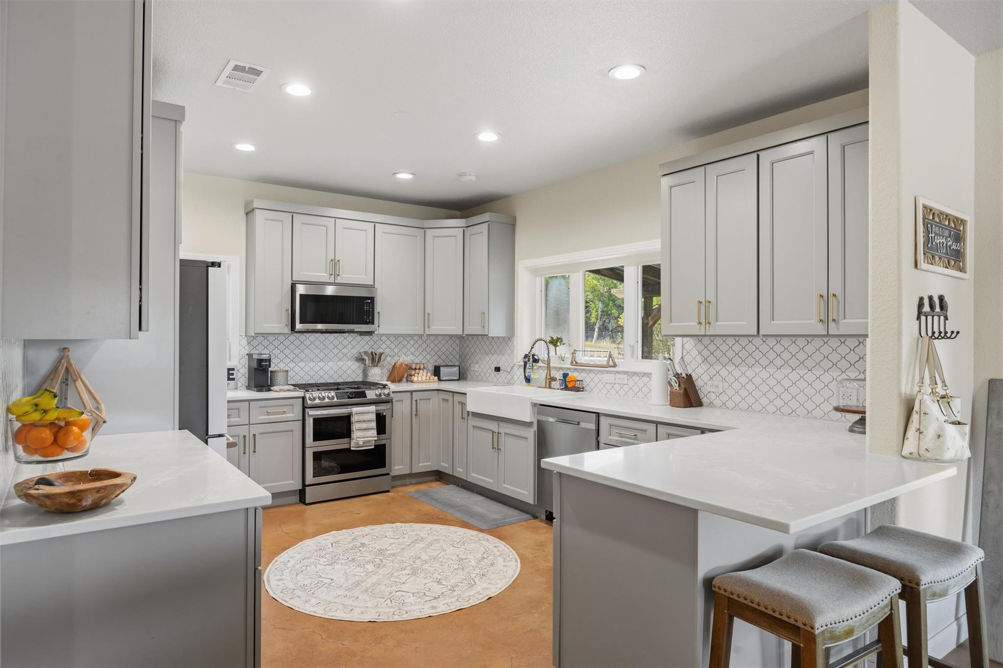 Kitchen with gray cabinets, patterned backsplash, farmhouse sink, and a large island with stools.