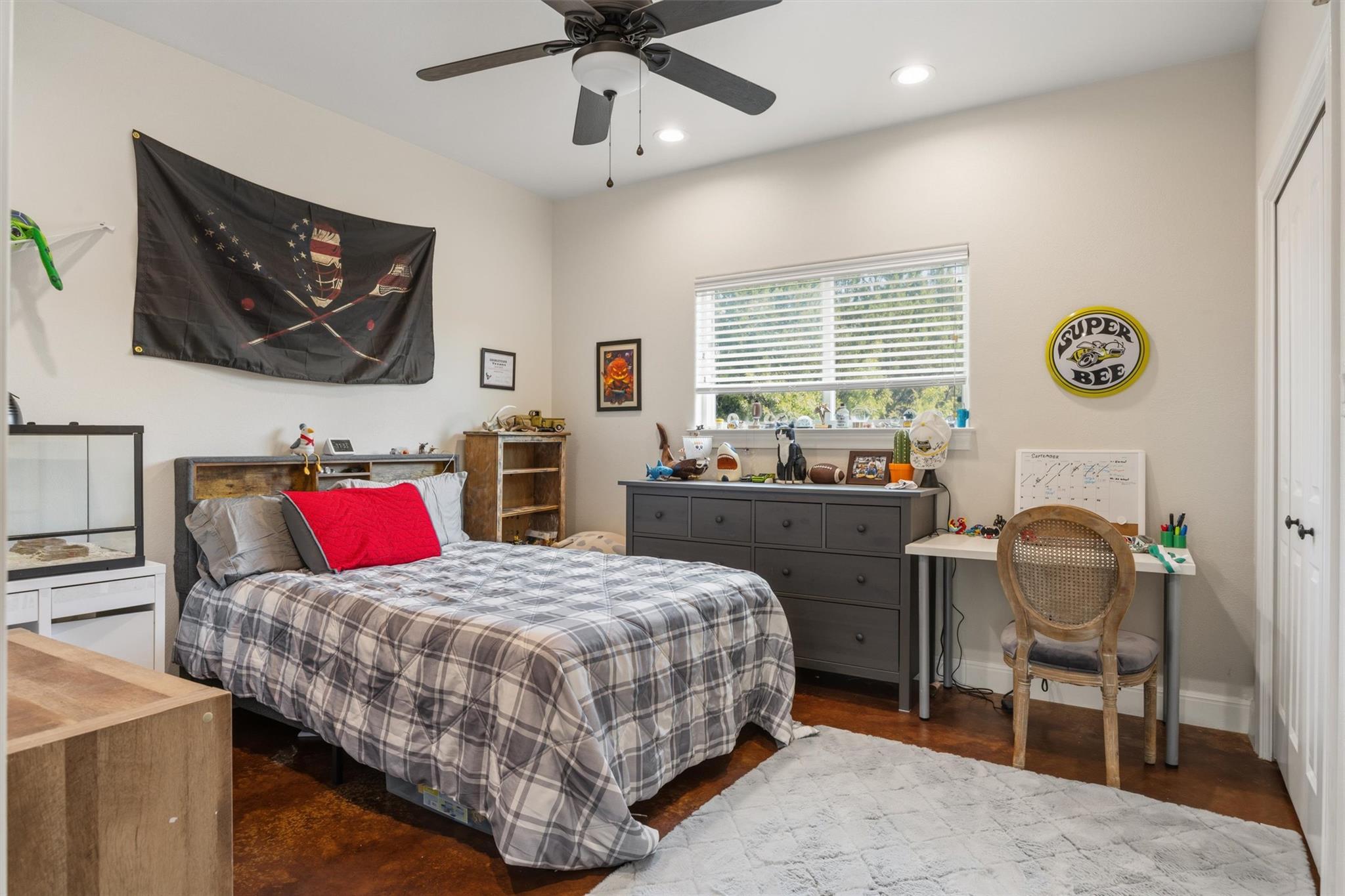 Bedroom with a plaid bed, dark dresser, desk, and round Super Bee wall sign.