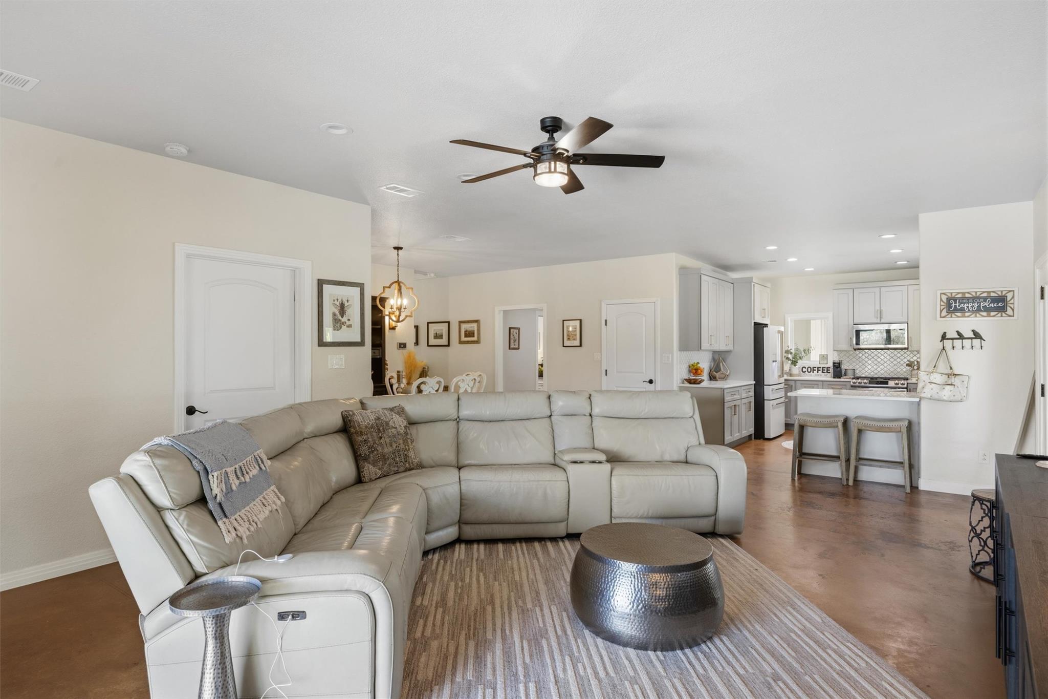 Open-plan living room with a white sectional sofa and kitchen island with two stools.