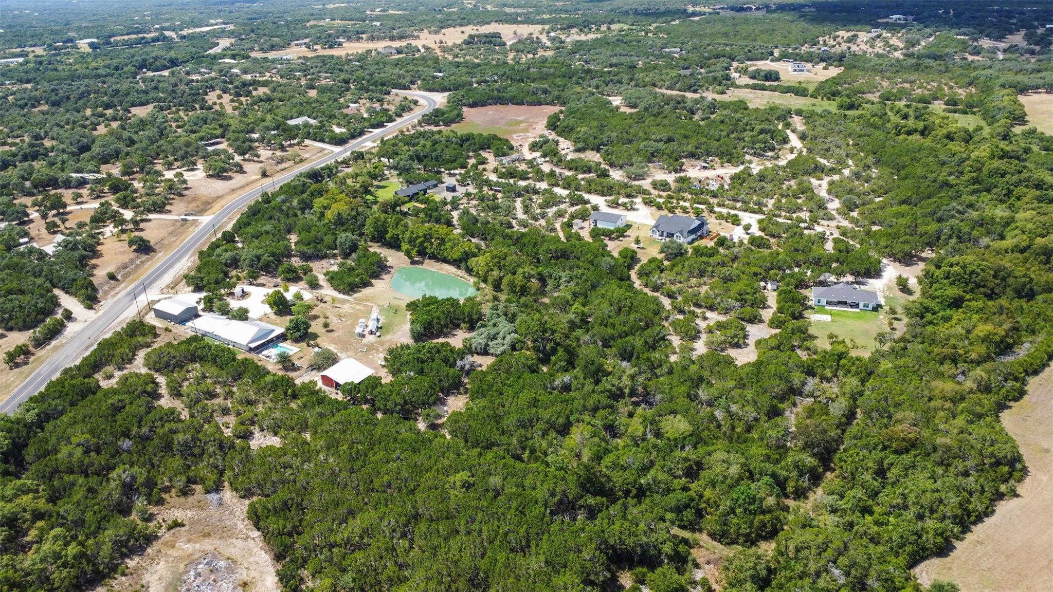 Aerial view of wooded rural acreage with scattered homes, a winding road, and a small pond.
