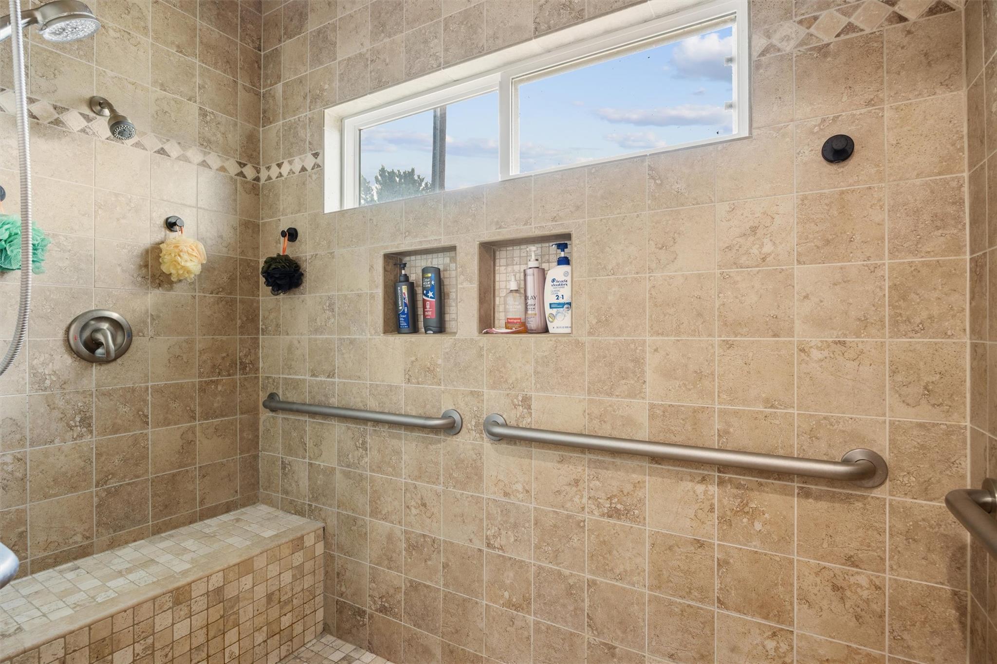 Walk-in tiled shower with a built-in bench, recessed niches, and long stainless-steel grab bars.