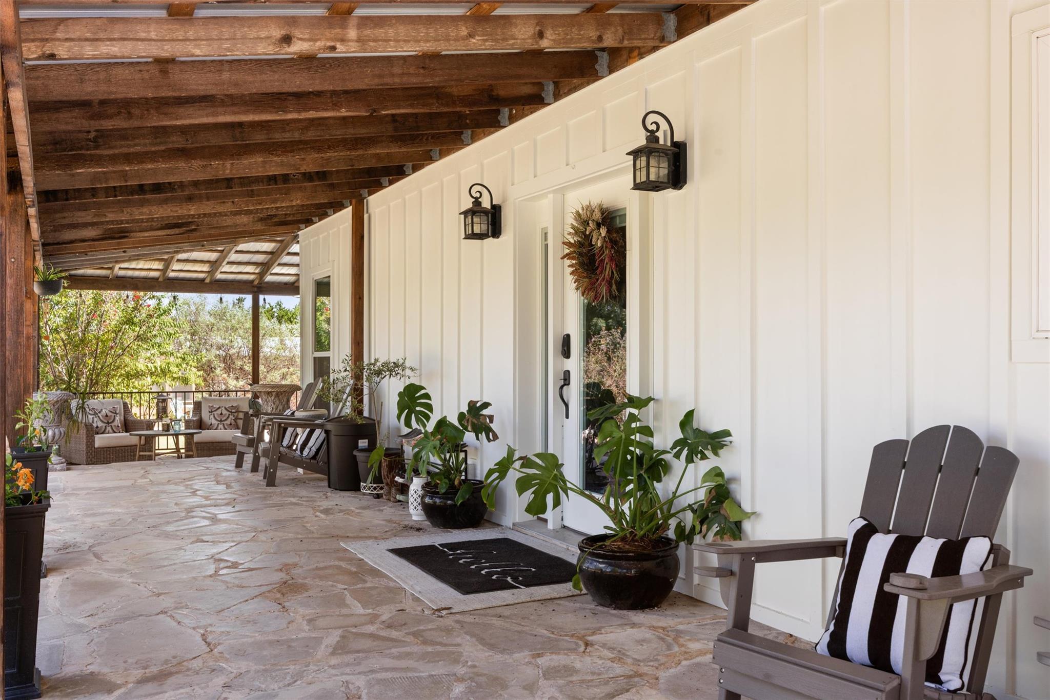Covered front porch with exposed timber beams, flagstone flooring, potted plants, and outdoor seating.