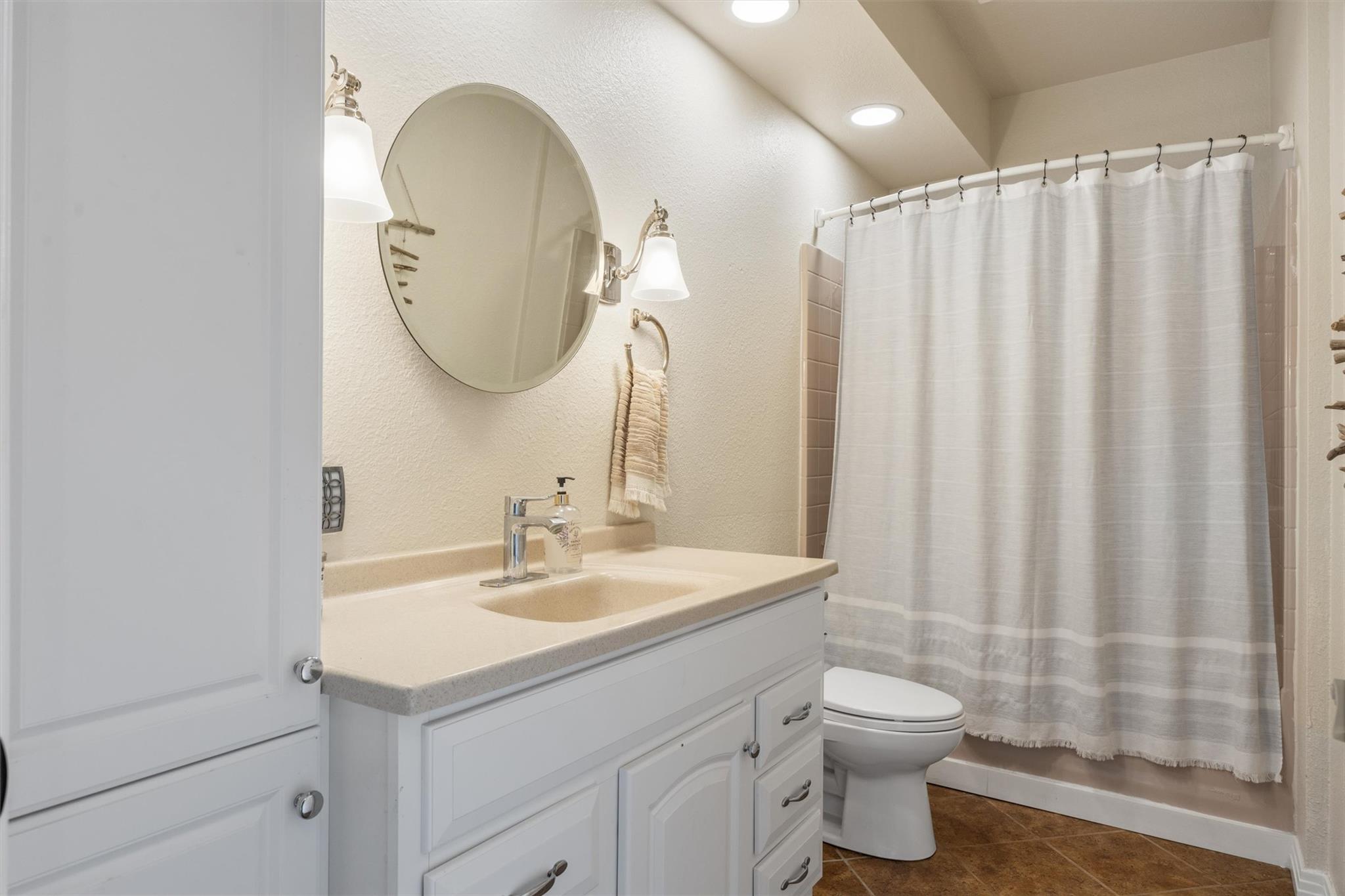 Bathroom with a white vanity, oval mirror, and shower curtain beside the toilet.