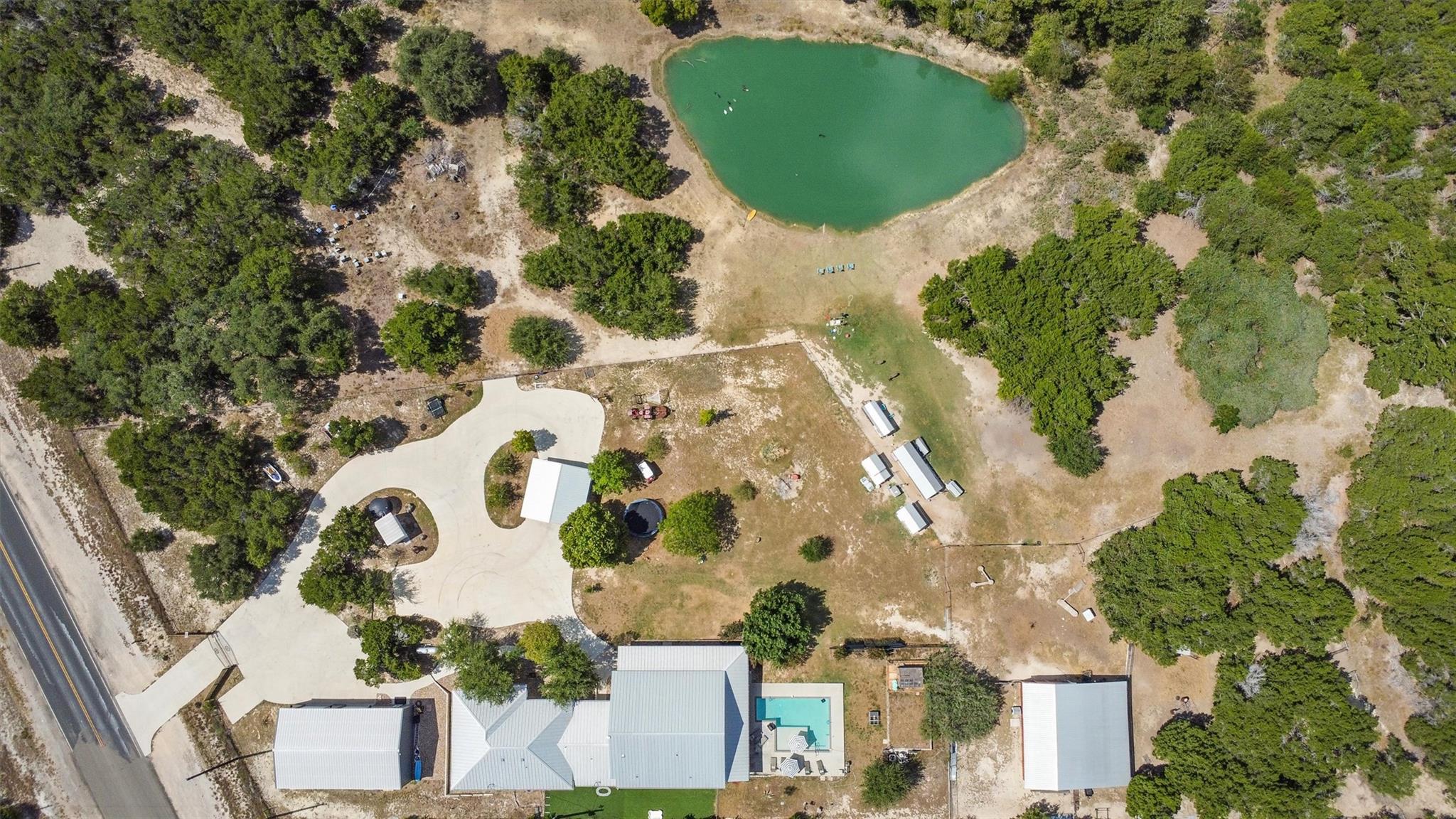 Aerial view of a wooded property with a pond, swimming pool, and several buildings.