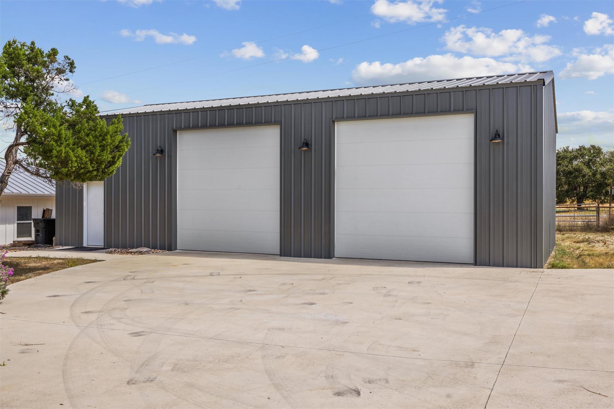 Gray metal outbuilding with two white garage doors and a broad concrete driveway.