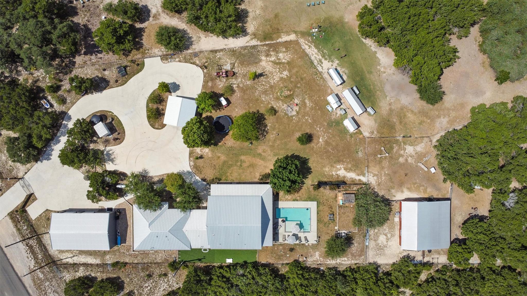 Aerial view of a rural home with a swimming pool, curved driveway, and multiple outbuildings.