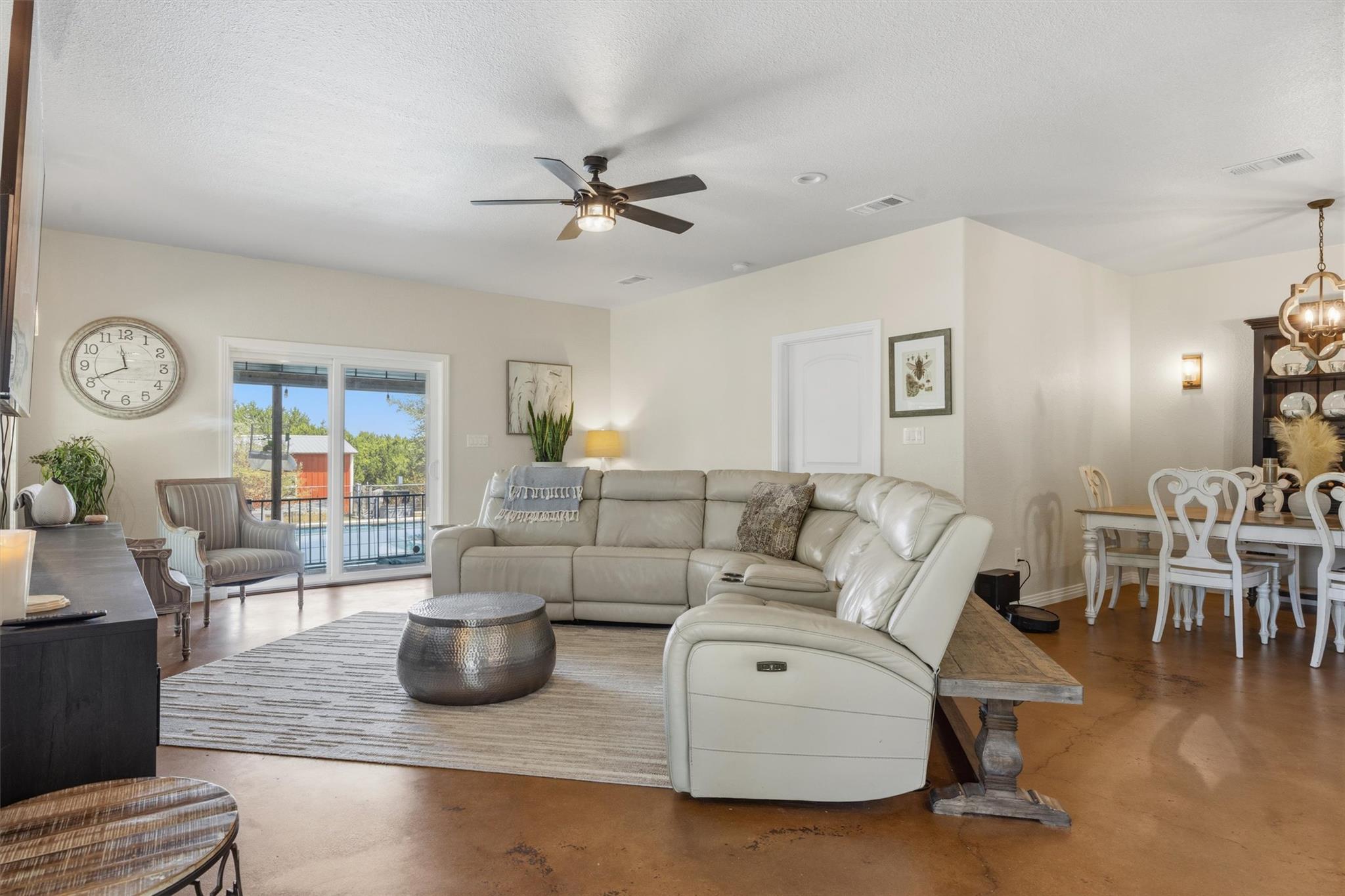 Living room with a cream sectional, concrete floors, and sliding doors overlooking a pool.