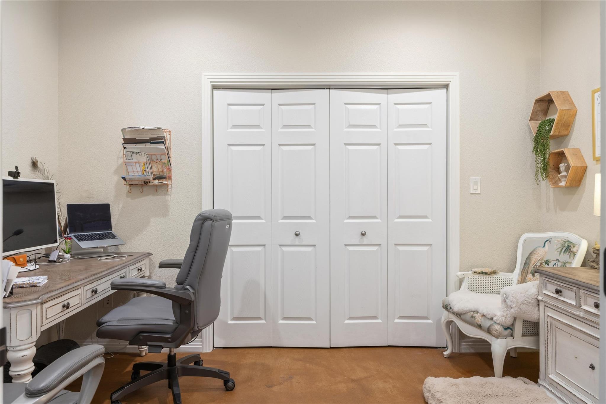 Home office with a computer desk, gray office chair, and white paneled closet doors.