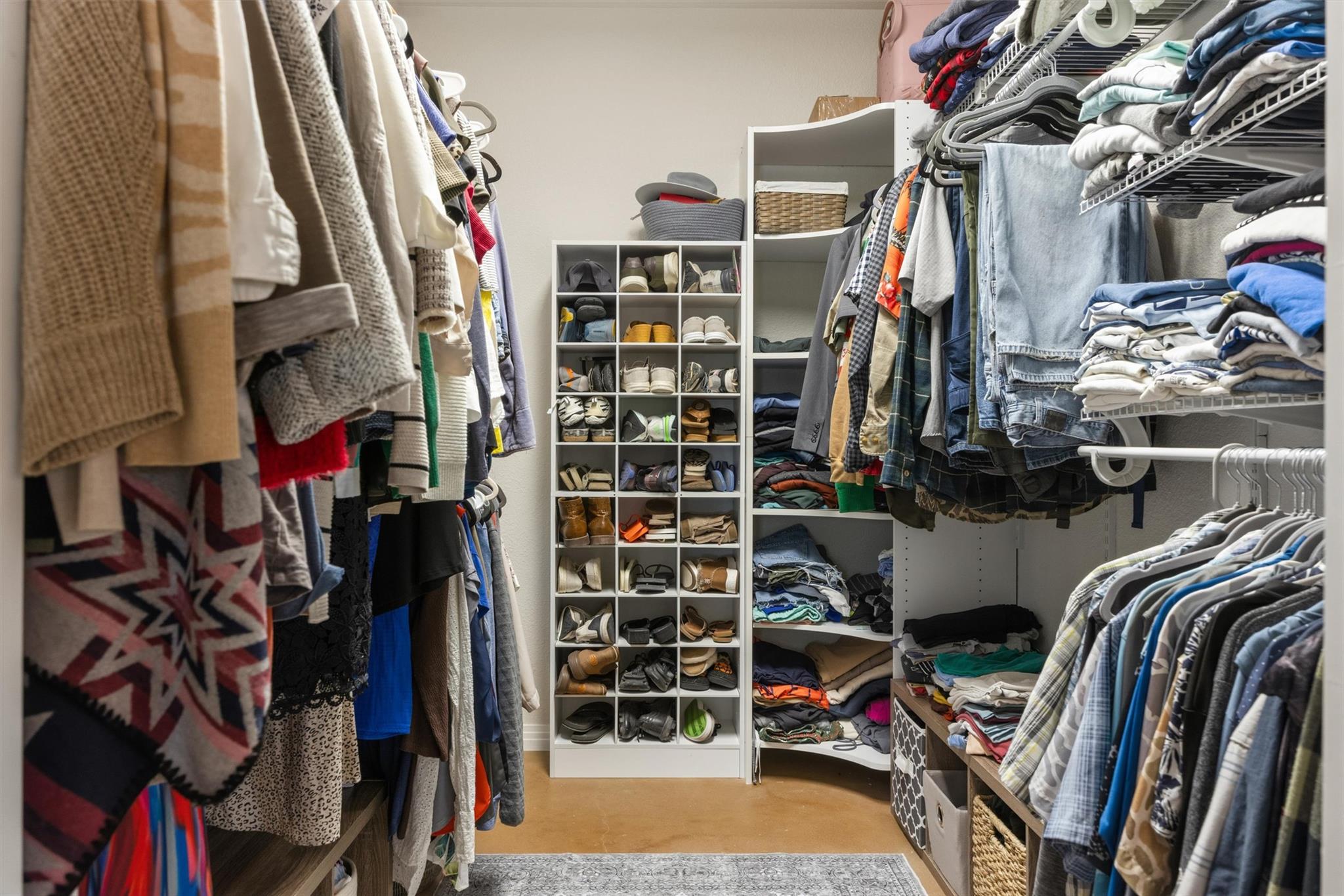 Walk-in closet with rows of hanging clothes, folded garments, and a central shoe-storage cubby.