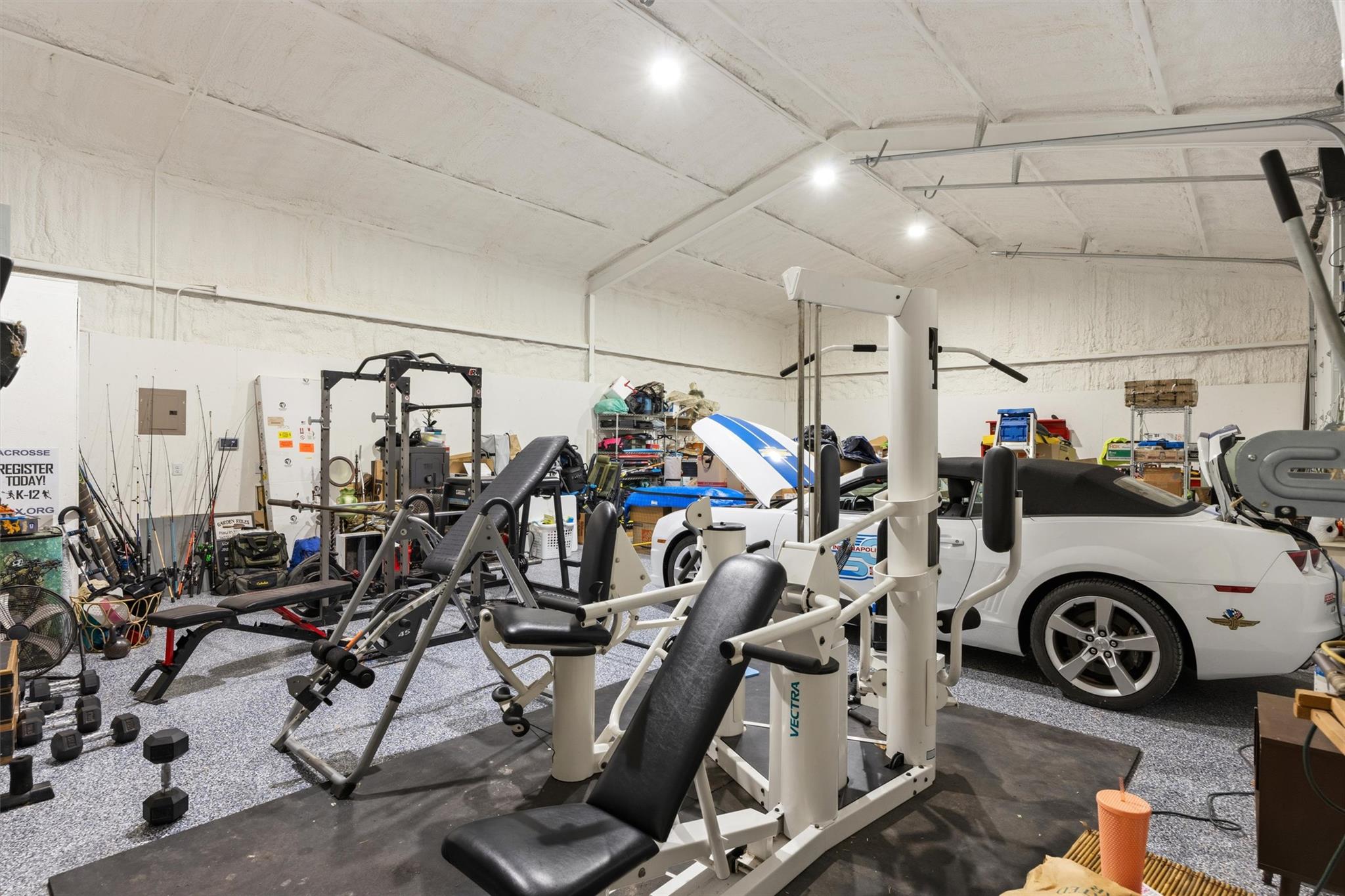 Home gym with weight machines and benches surrounding a white sports car.