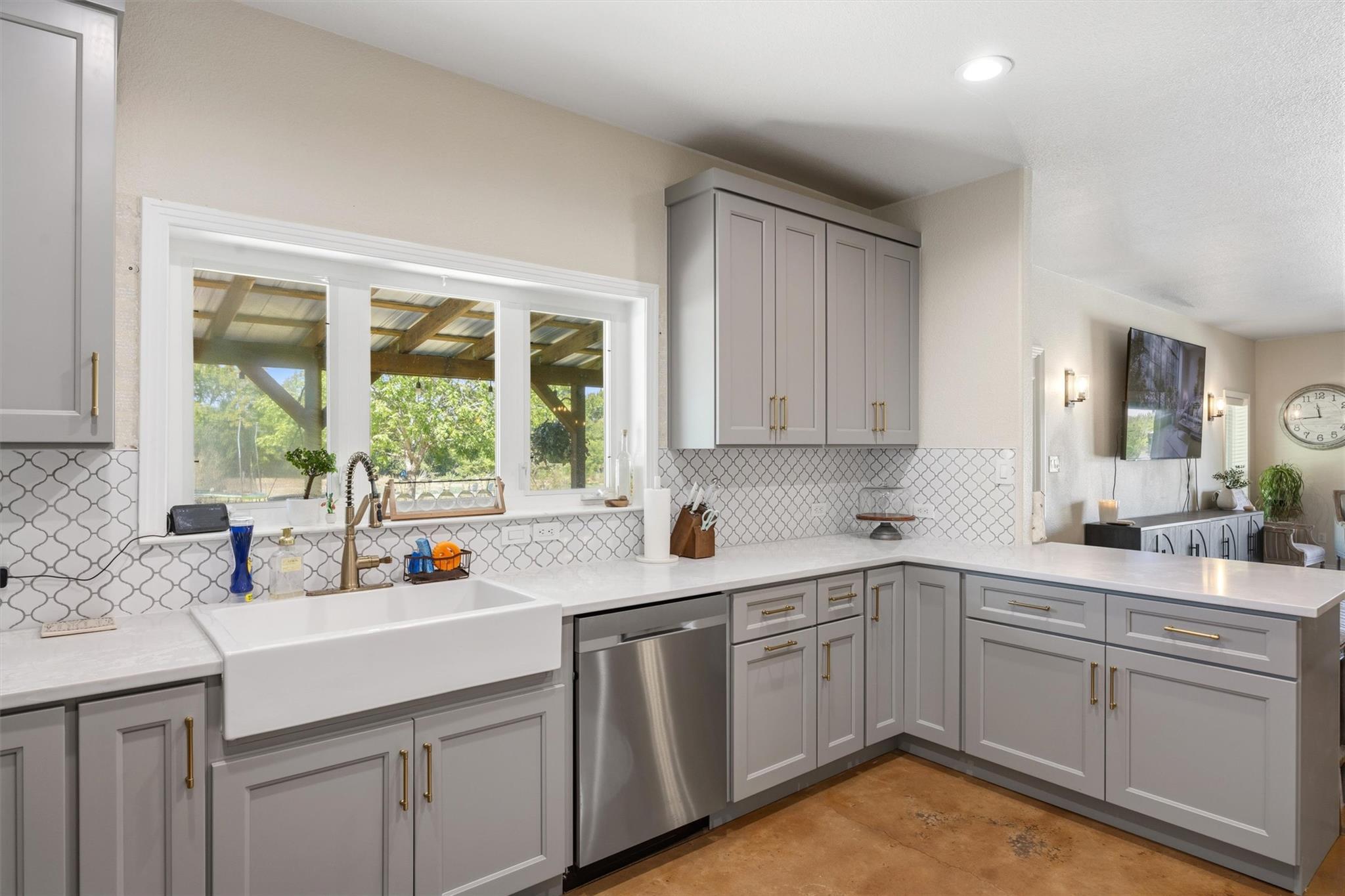 Kitchen with gray cabinets, farmhouse sink, patterned tile backsplash, and windows overlooking a covered patio.