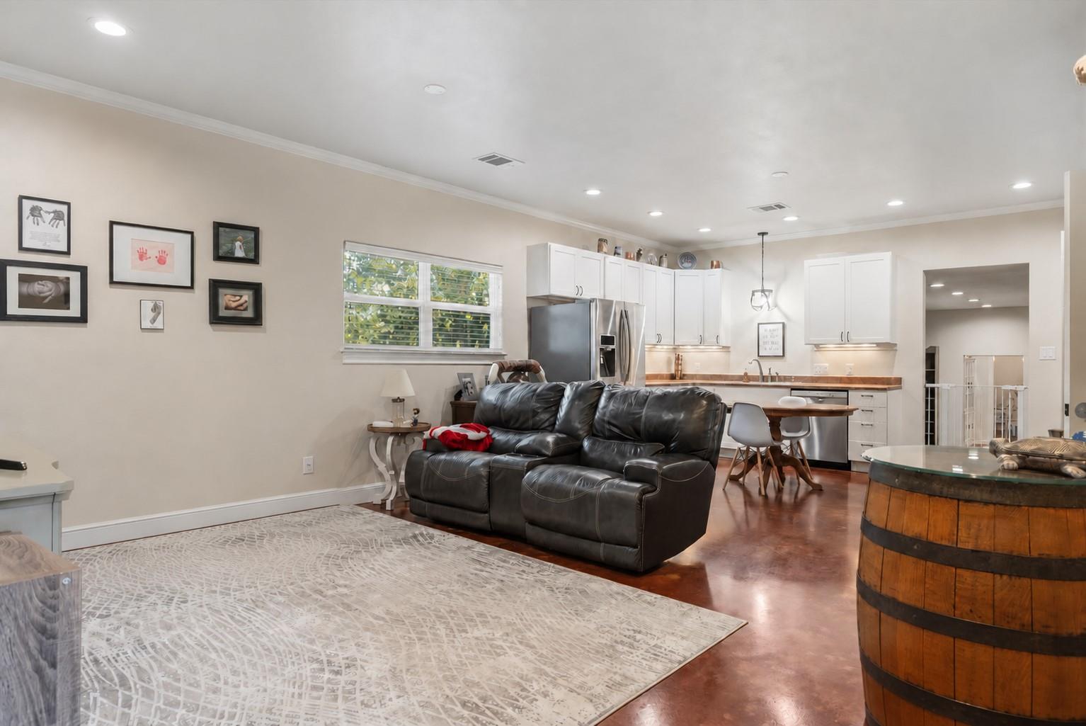 Open-plan living room and kitchen with a dark leather sofa, white cabinets, and polished reddish floors.
