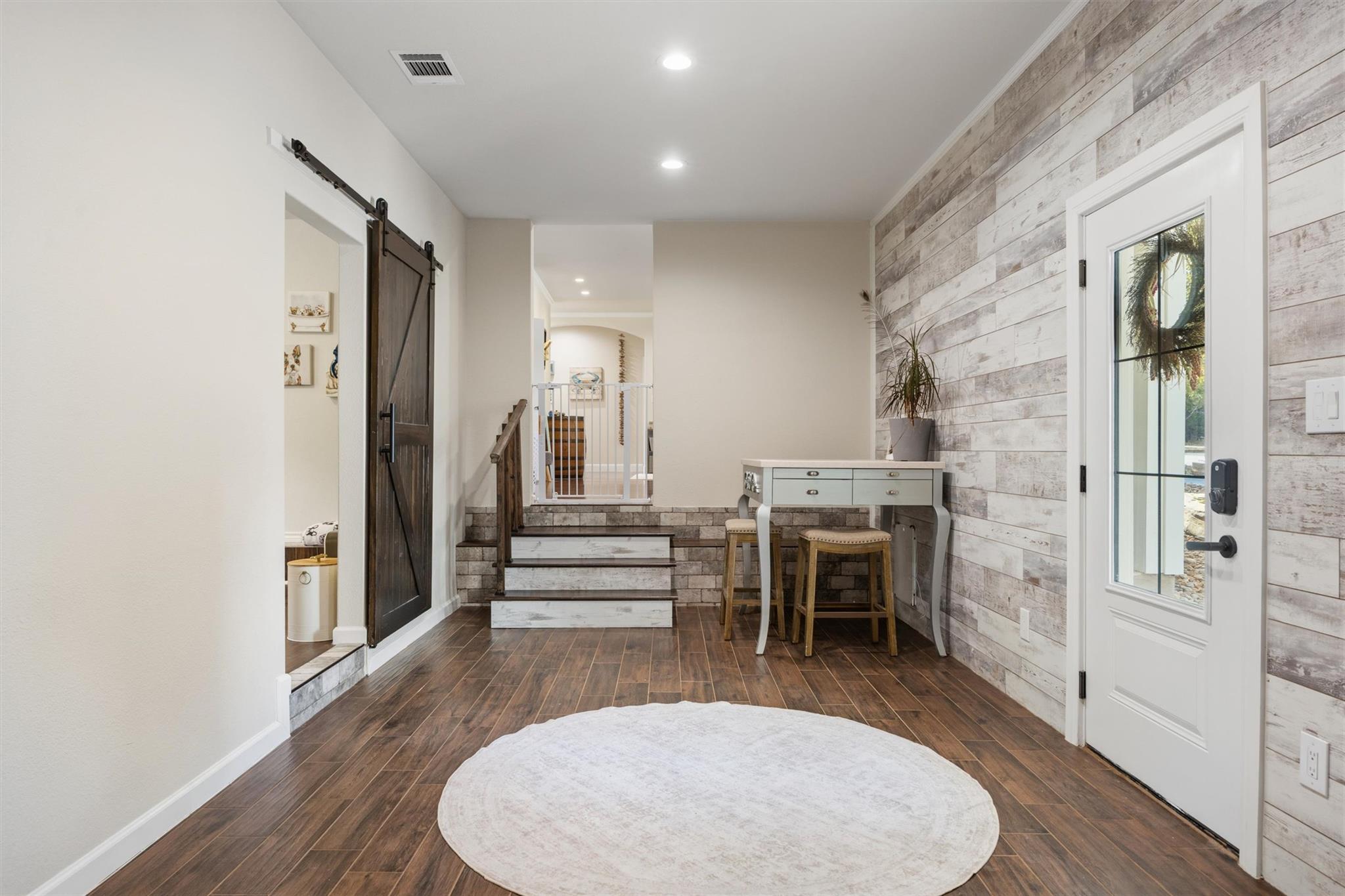 Entryway with a dark sliding barn door, staircase, and light wood-plank accent wall.