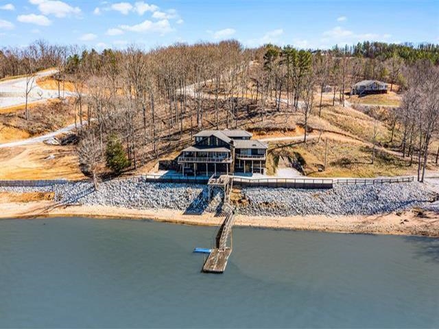 Lakefront home with a long dock, rocky shoreline, and leafless trees.