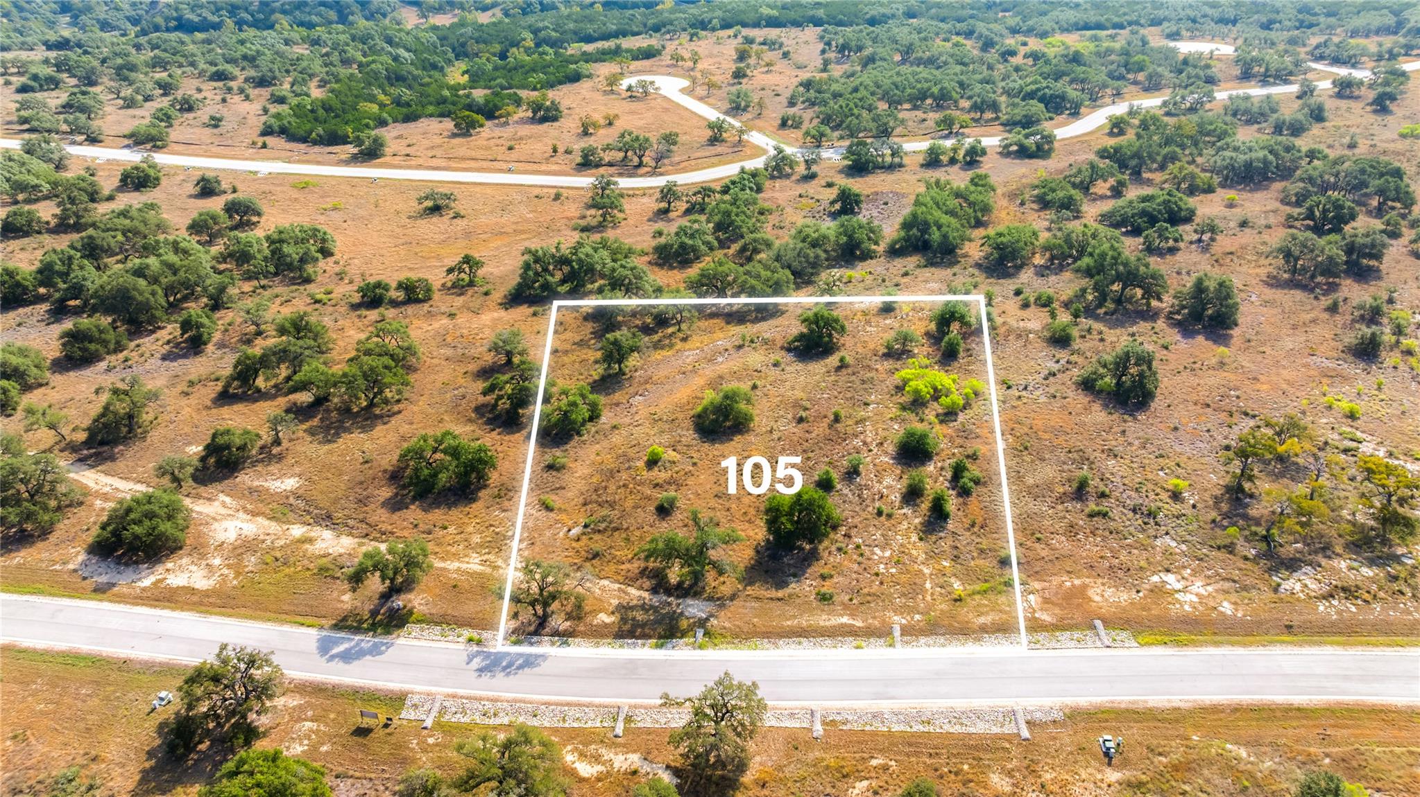 Aerial view of Lot 105, outlined beside a paved road amid dry grass and scattered oak trees.