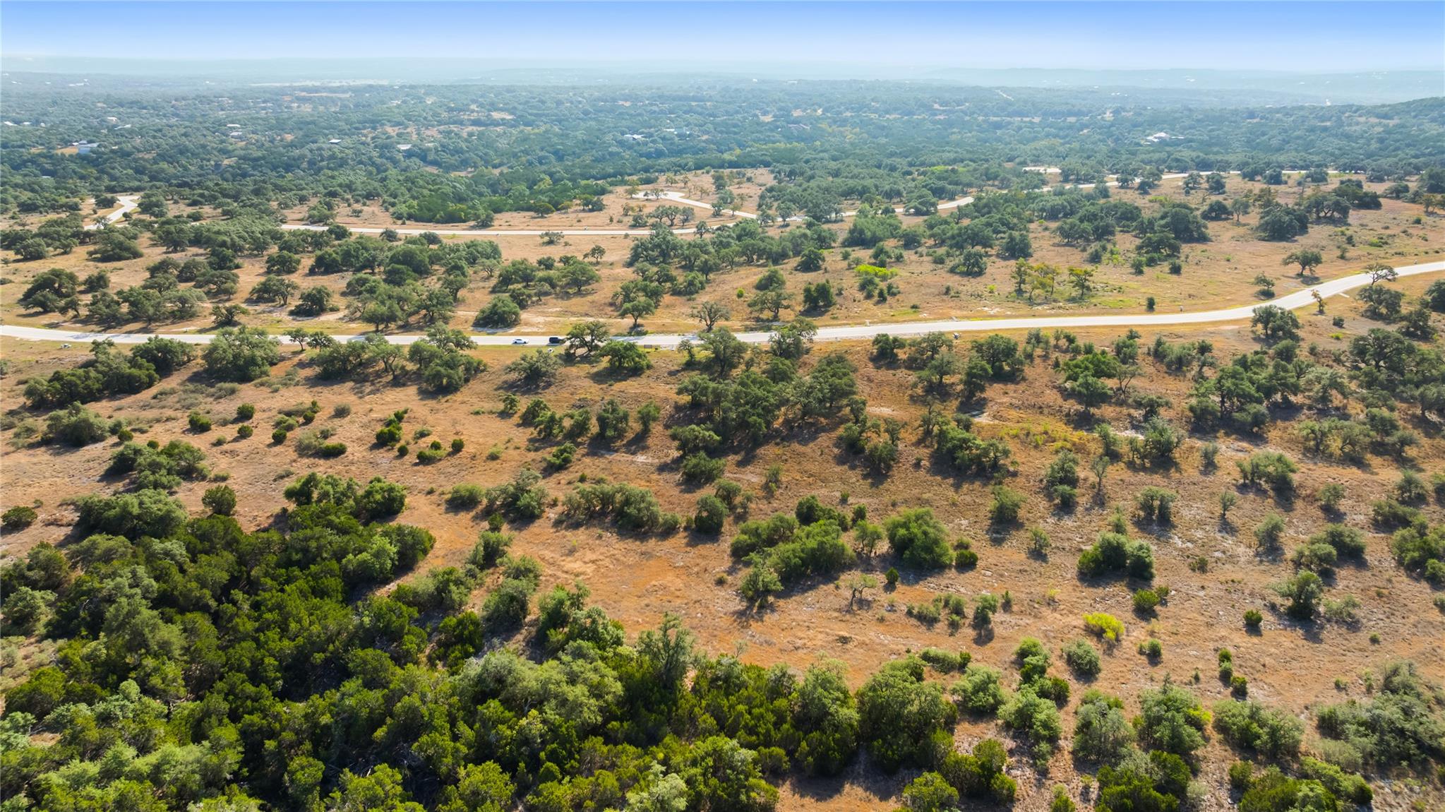 Aerial view of undeveloped Texas land with scattered trees, brush, and a paved road.
