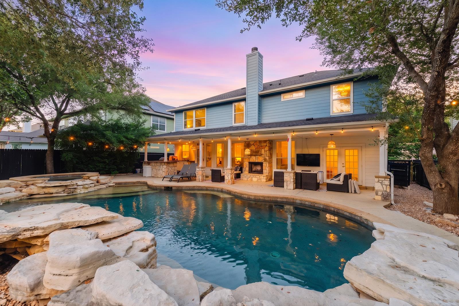 Two-story home's rear exterior with stone-edged pool and illuminated covered patio at dusk.