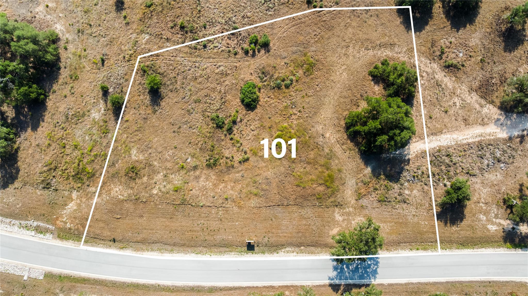 Aerial view of vacant Lot 101, outlined in white beside a paved road.
