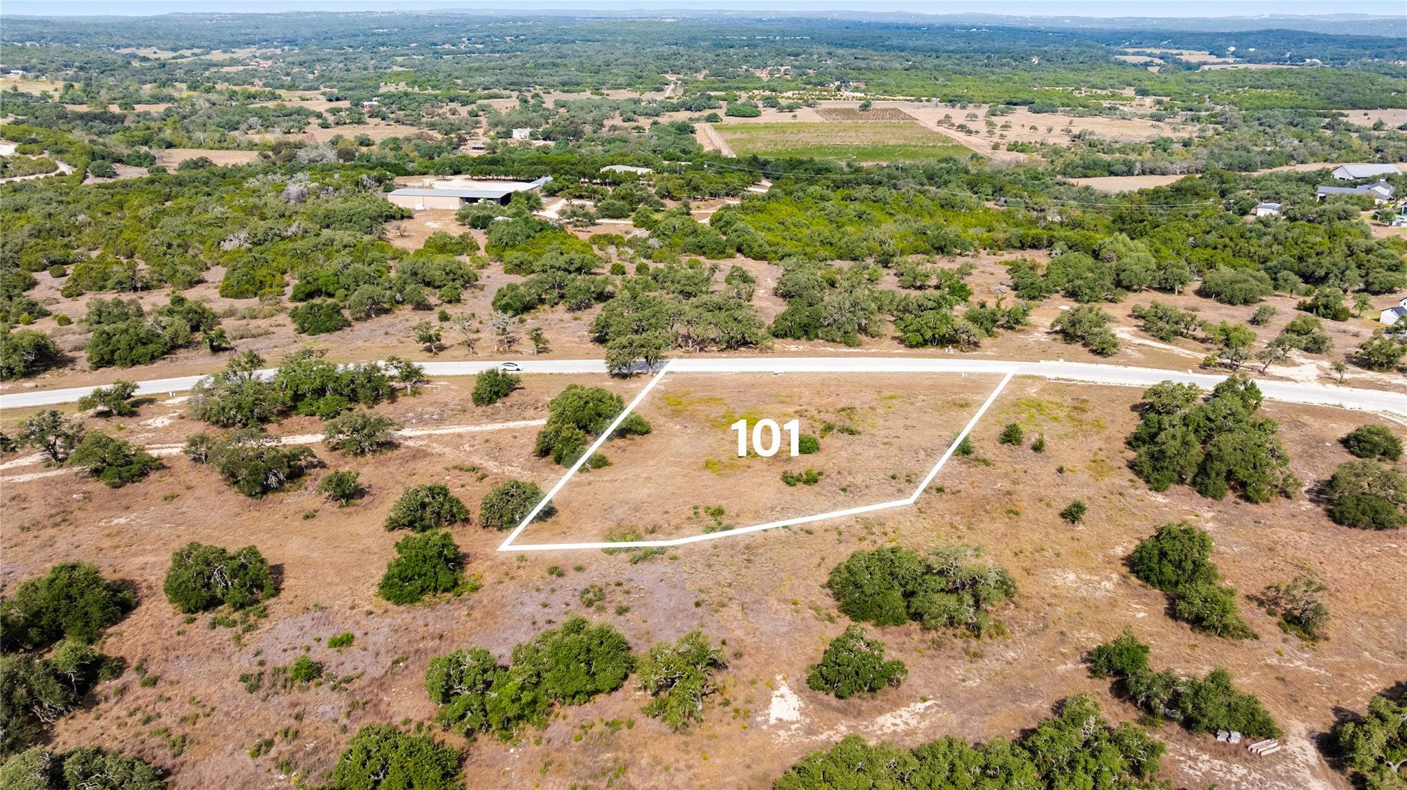 Aerial view of vacant lot 101, outlined in white beside a road amid dry brush and scattered trees.