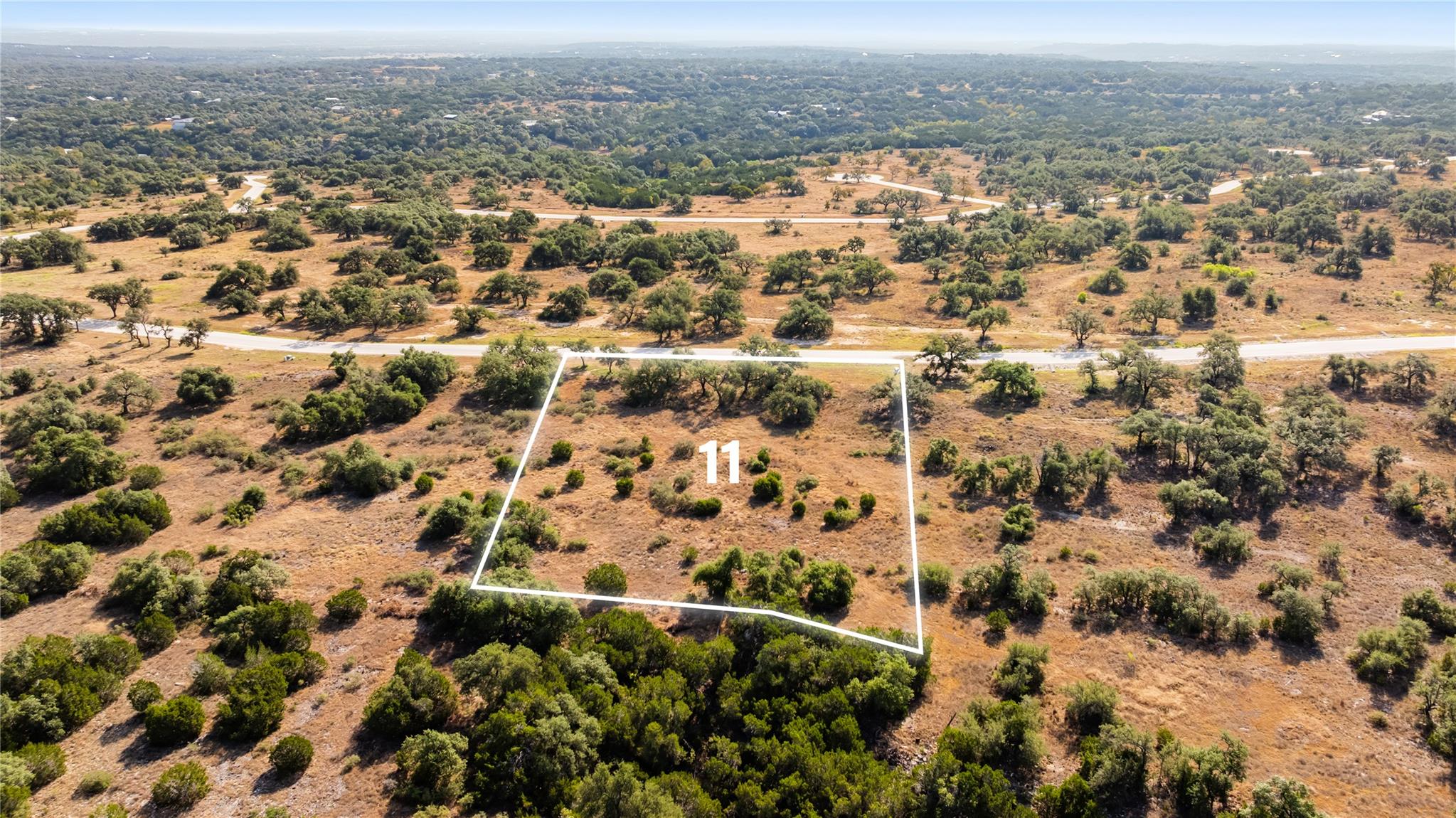 Aerial view of vacant Lot 11 outlined among trees beside a paved road.