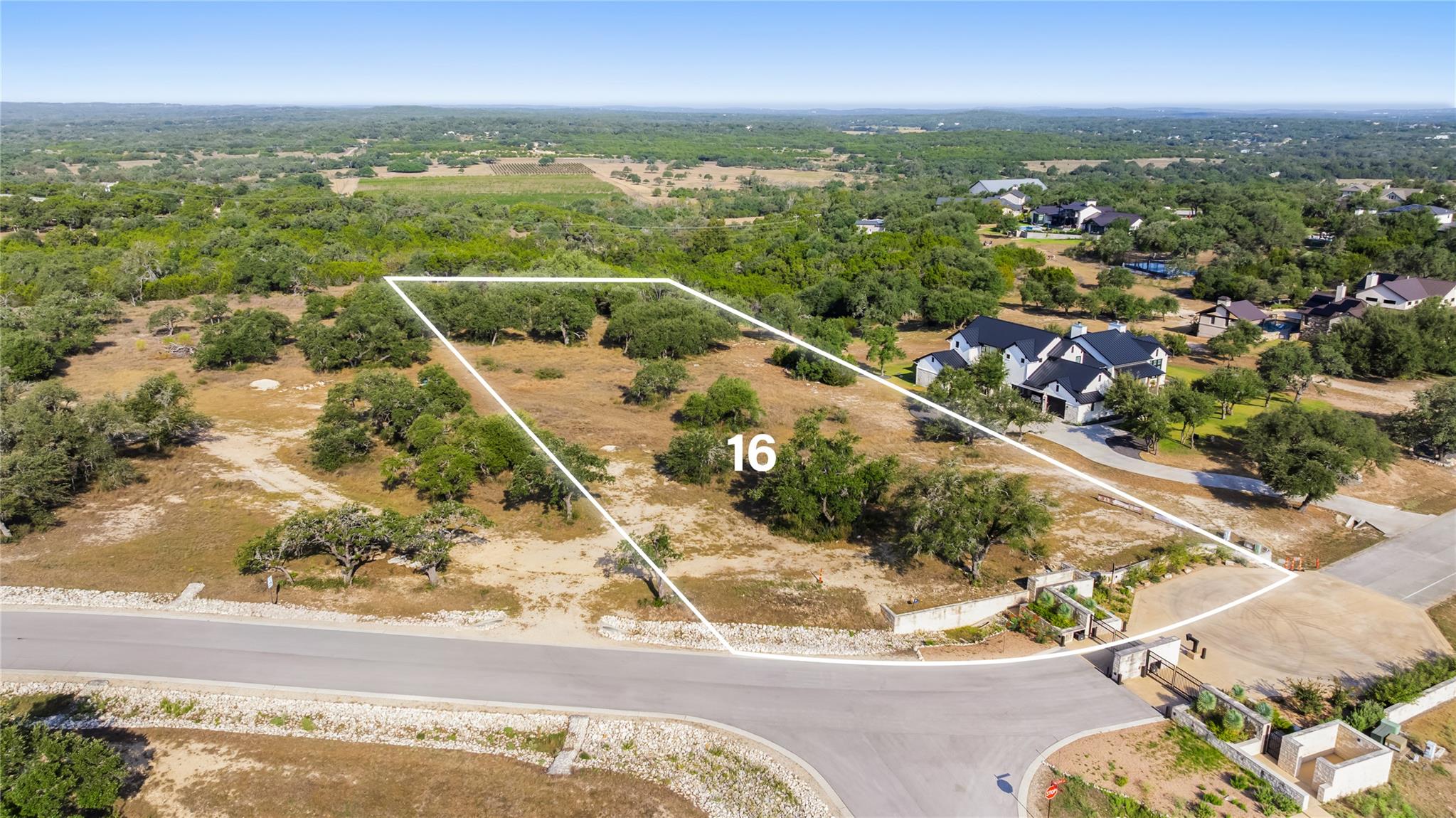 Aerial view of vacant Lot 16, outlined in white among trees beside a residential road.
