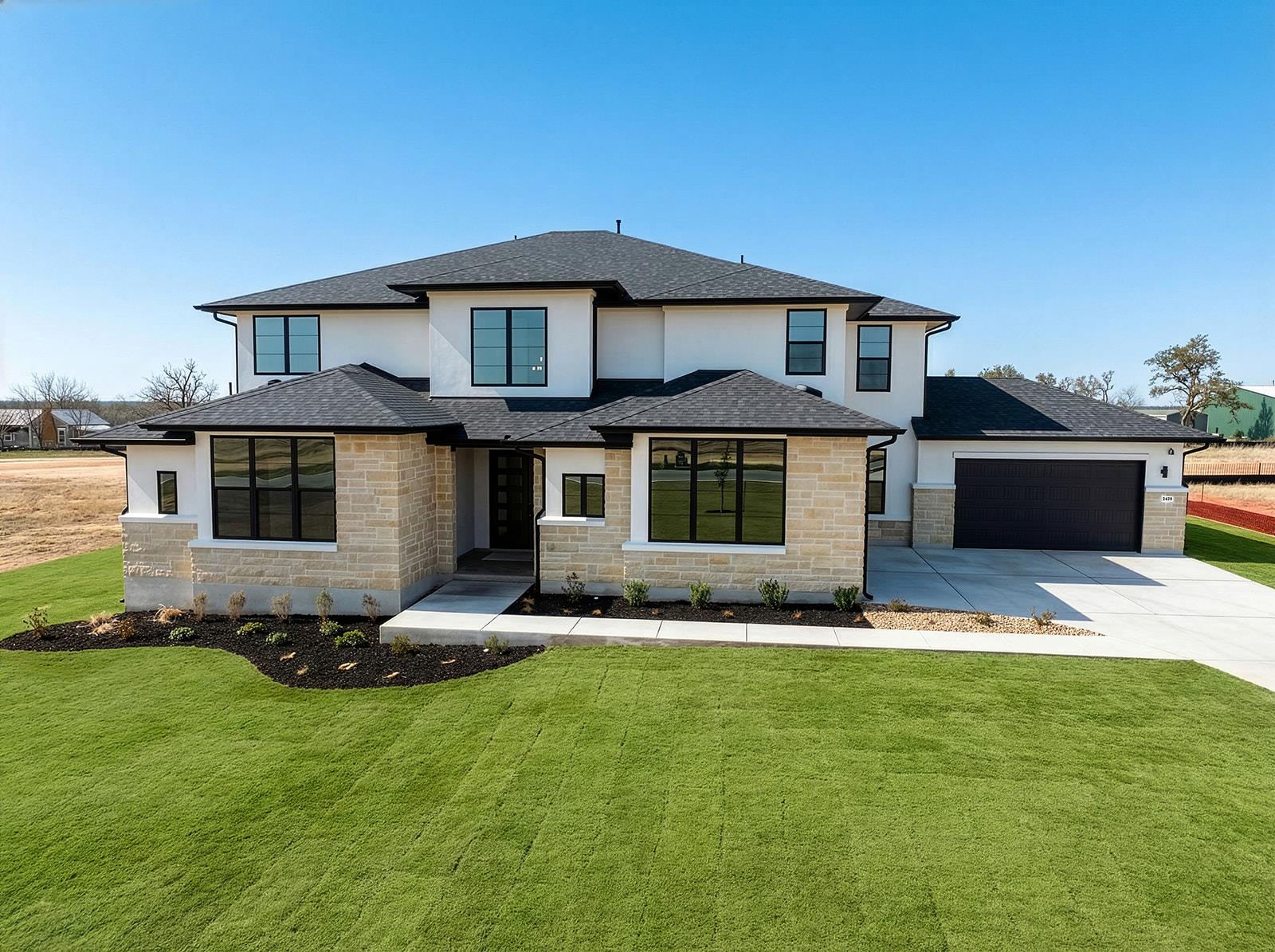 Modern two-story house with stone facade, dark roof, attached garage, and broad green lawn.