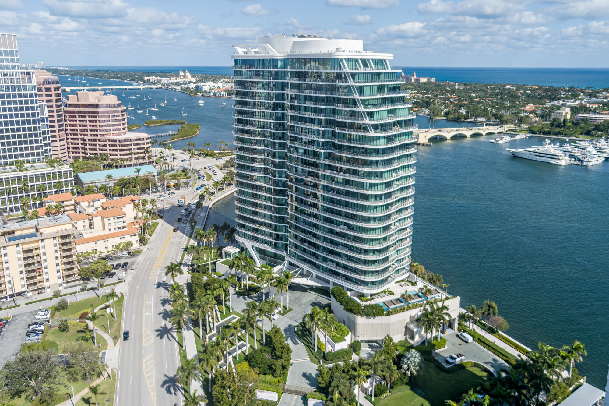 Waterfront condominium tower with curved glass balconies, marina, boats, and bridge