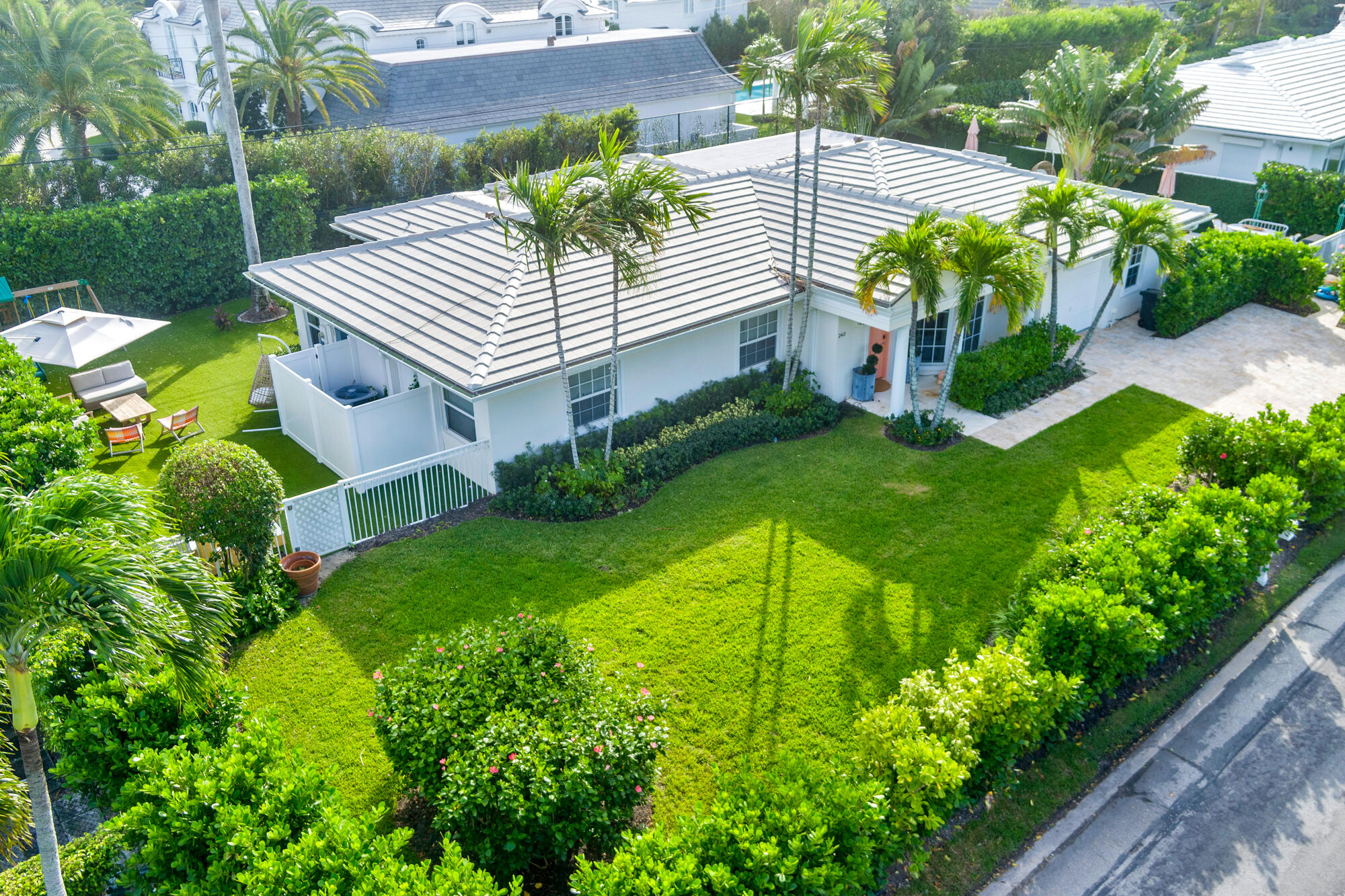 Aerial view of a white tile-roofed home with palm trees, a lush lawn, and a paved driveway.