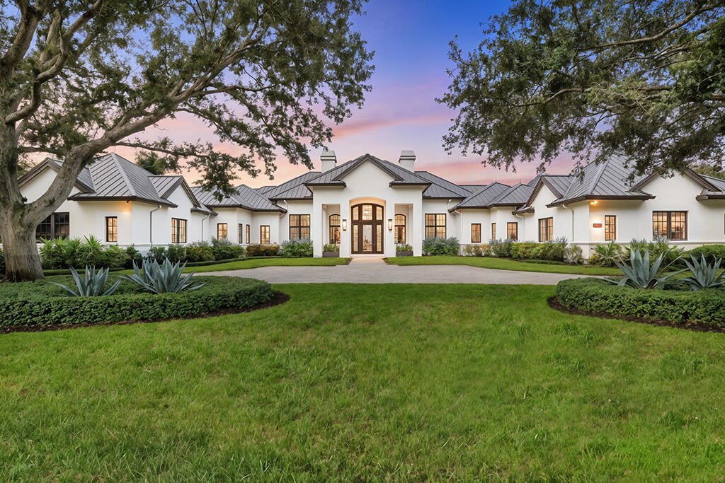 White estate with a metal roof framed by mature trees at dusk.