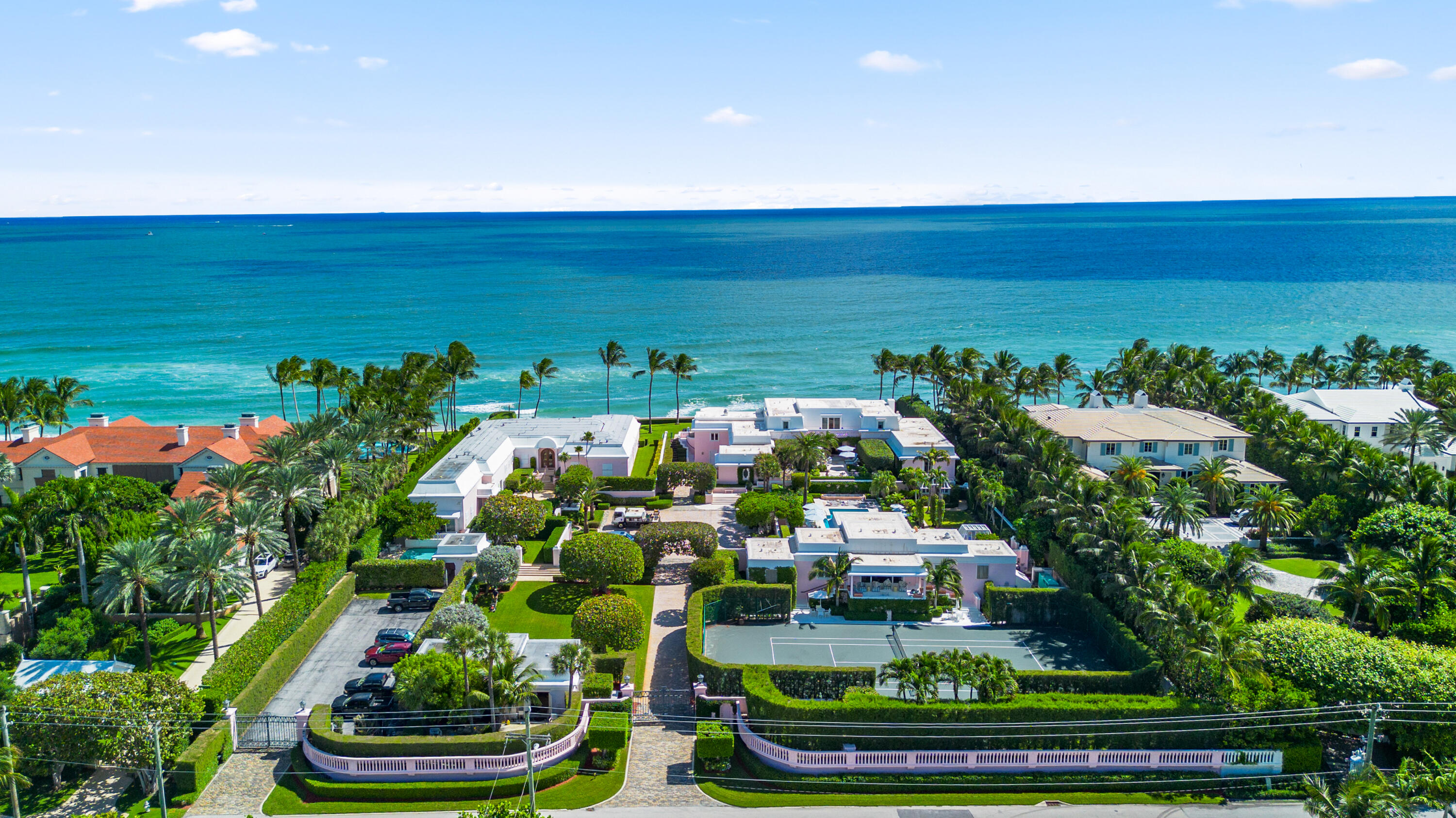 Aerial view of a landscaped beachfront estate with a tennis court and oceanfront palm trees.