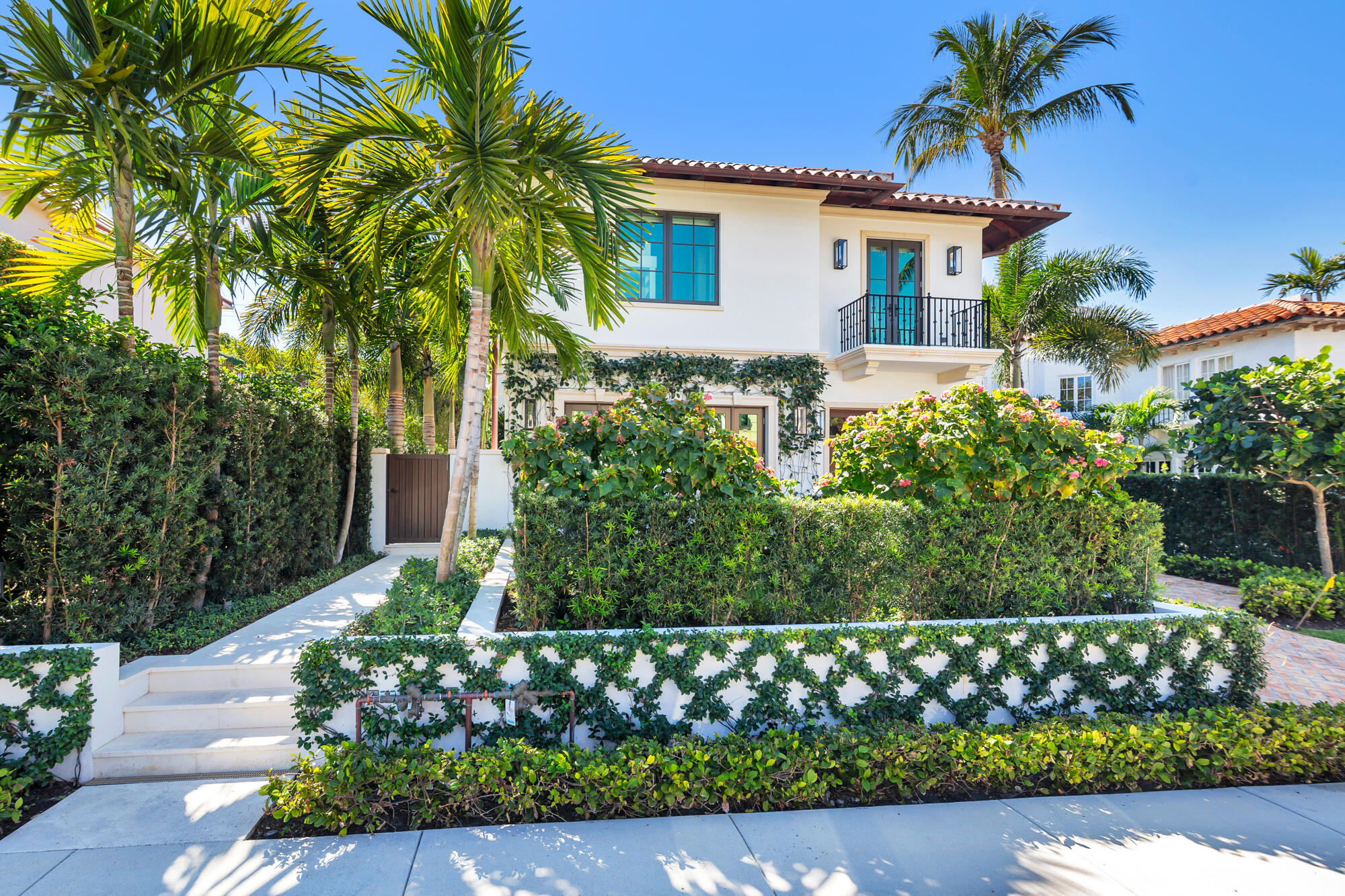 218 Everglade Avenue, a white stucco home with a balcony framed by palms and lush landscaping.