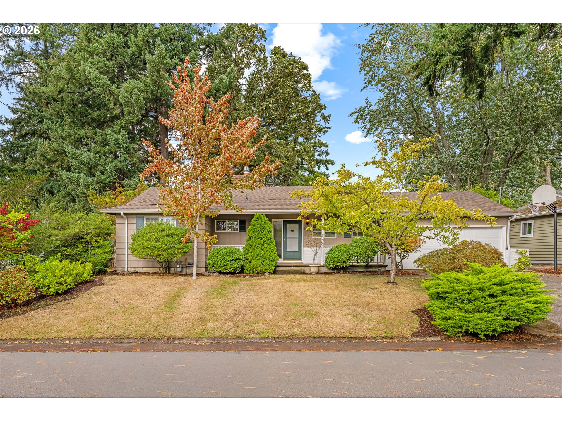 Single-story home with an attached garage, leafy landscaped yard, and basketball hoop by the driveway.