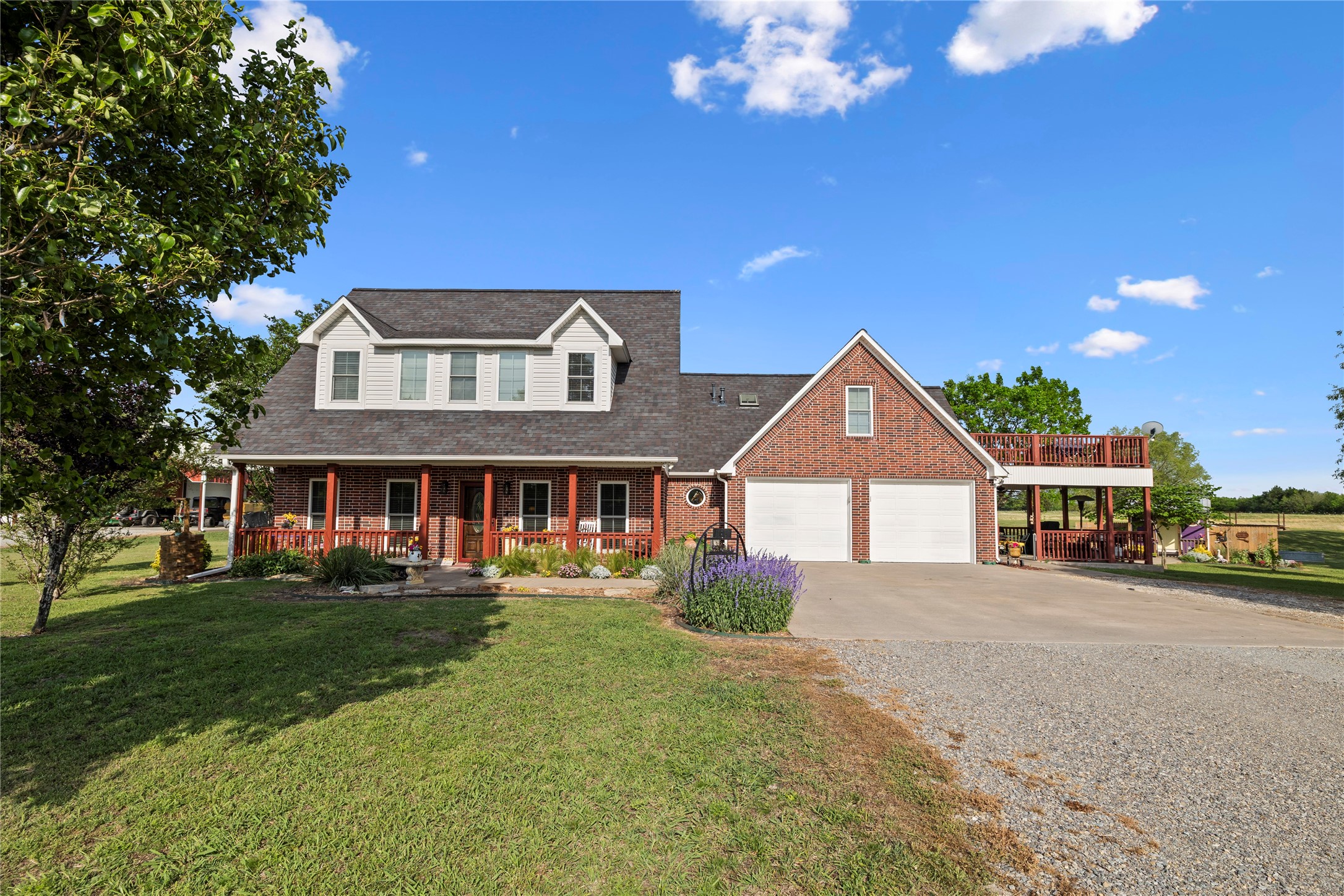 Red brick country home with a covered porch, two-car garage, and raised wooden deck.