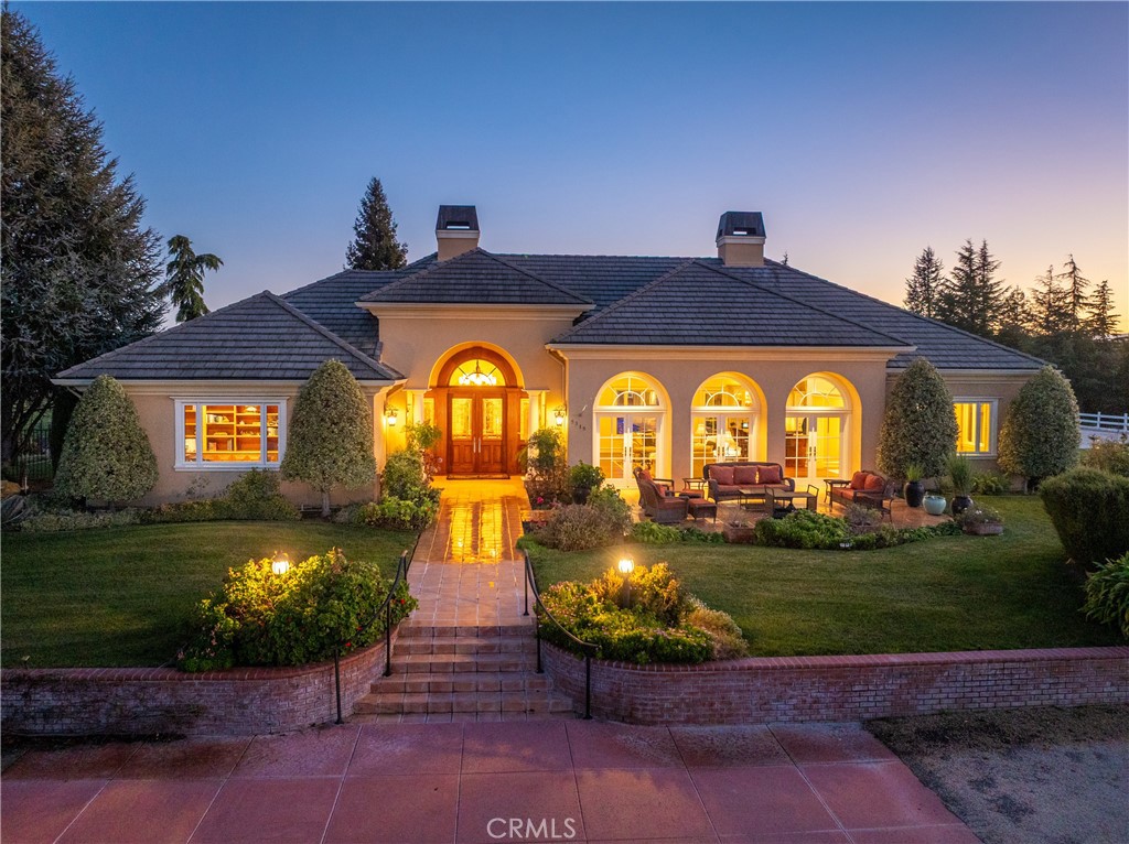 Single-story stucco home with arched lit windows, tiled walkway, and landscaped front patio at dusk.
