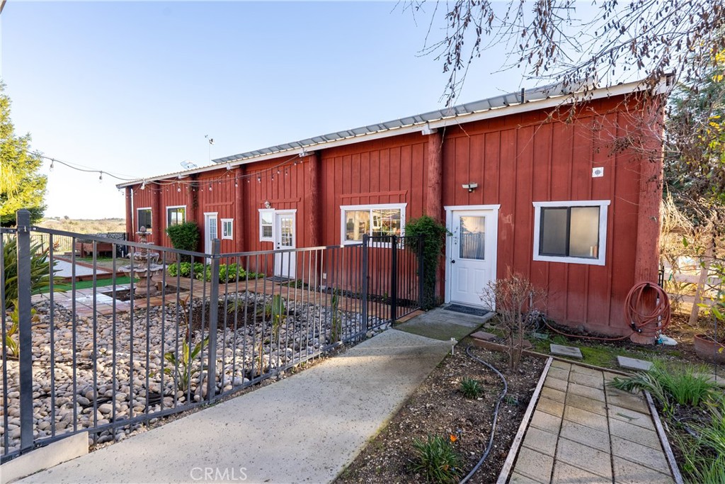 Red-sided property exterior with a white entry door, black metal fence, and stone-covered patio.