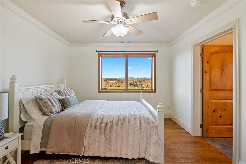 Bedroom with a white bed, ceiling fan, and countryside visible through a wood-framed window.