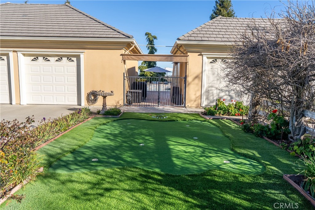 Backyard putting green between two garage wings, with garden beds and a gated entrance.