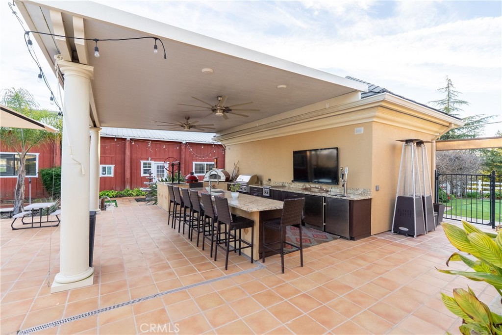 Covered outdoor kitchen with a long island, bar stools, built-in grill, and ceiling fans.
