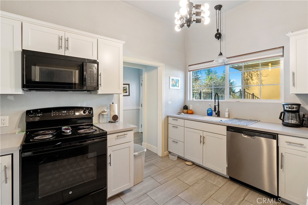 Kitchen with white cabinets, black range, stainless steel dishwasher, and a large sunlit window.