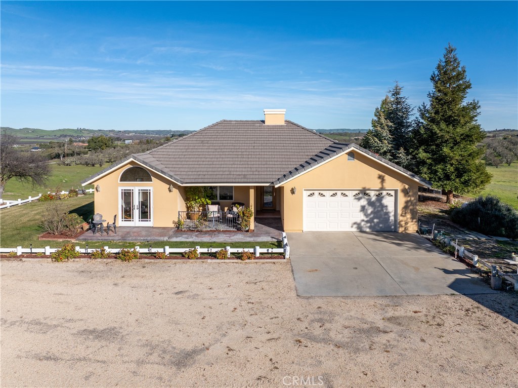 Single-story tan home with an attached garage, white fence, and rolling countryside beyond.