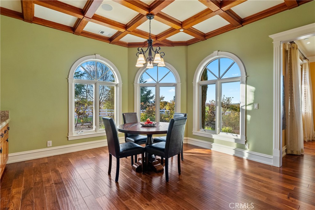 Dining room with a round table, polished hardwood floors, and three tall arched windows.