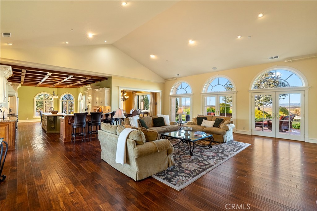 Living room with vaulted ceiling, arched windows, hardwood floors, and an adjoining kitchen.