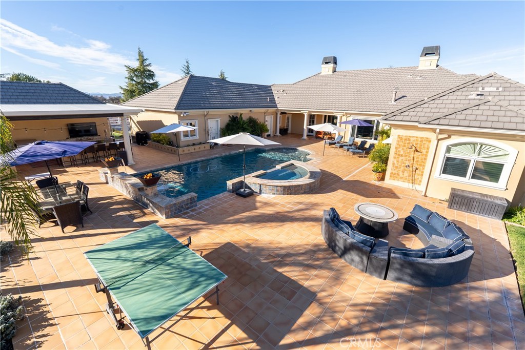 Backyard pool and raised spa surrounded by a tiled patio with outdoor seating and a ping-pong table.