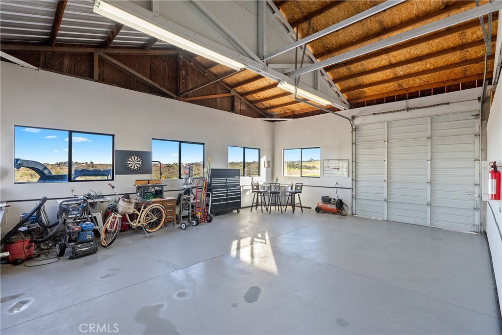 Spacious garage workshop with exposed beams, tools, bicycles, and large roll-up doors.