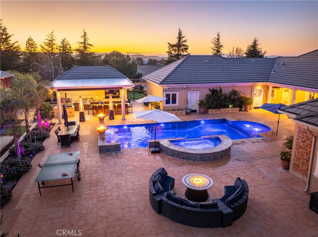 Backyard pool and spa with a covered outdoor kitchen and fire pit seating at dusk.