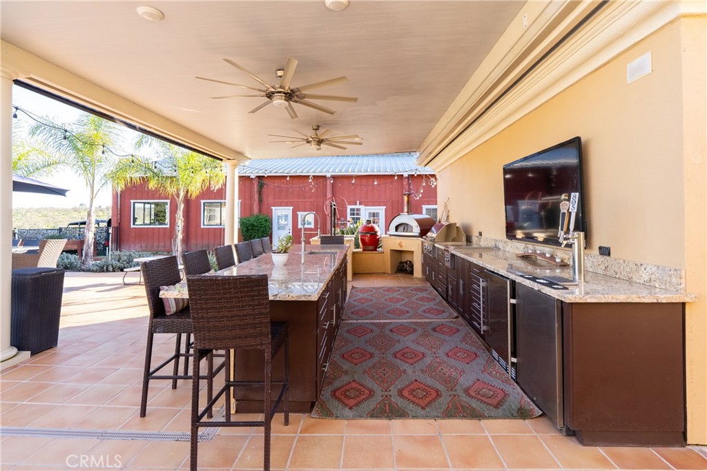 Covered outdoor kitchen with granite counters, bar seating, built-in grill, and ceiling fans.