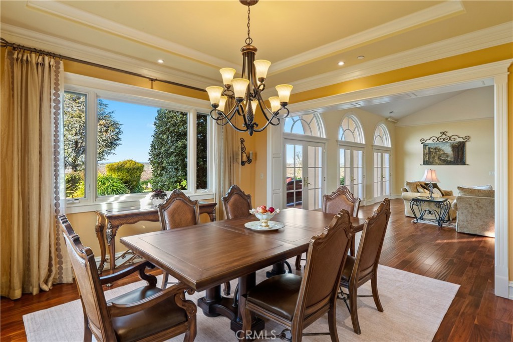 Dining room with a carved wood table, chandelier, large windows, and arched French doors.