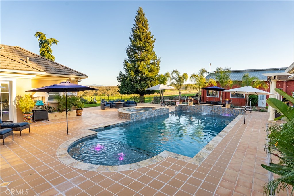 Outdoor swimming pool and raised spa surrounded by a tiled patio, seating, and umbrellas.